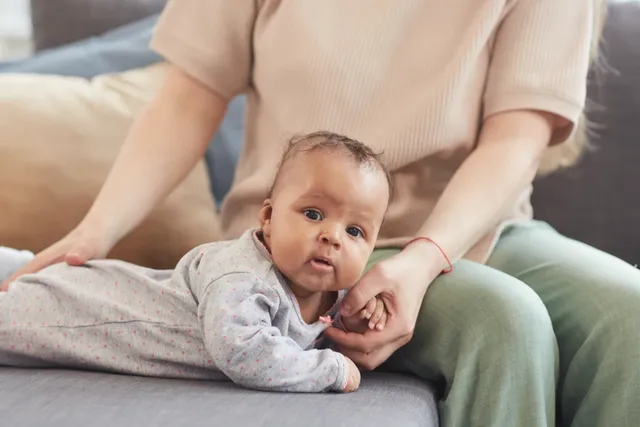 Baby liegt auf dem Bauch auf dem Sofa, gehalten von Elternteil