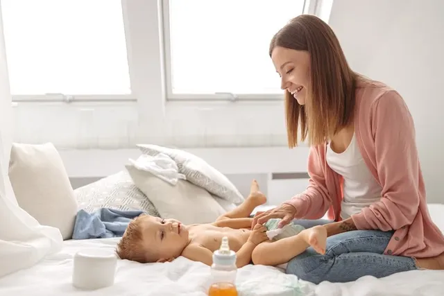 Mutter wechselt lächelnd Windel bei Baby auf dem Bett in hellem Schlafzimmer