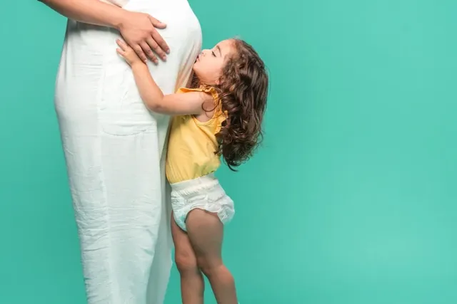Schwangerschaft: Kleines Mädchen umarmt den Babybauch der Mutter spielerisch.