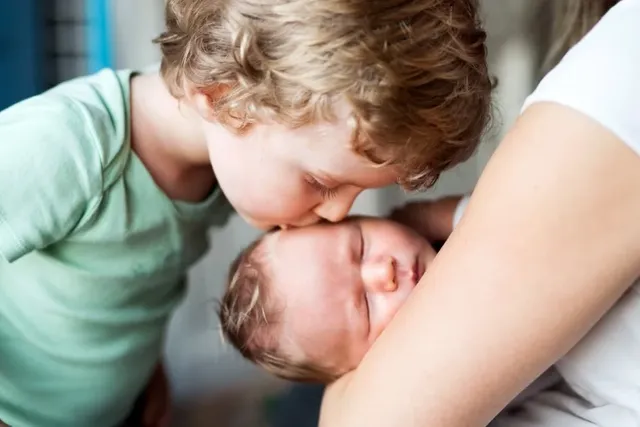 Kleiner Junge küsst Neugeborenes, gehalten von Mutter
