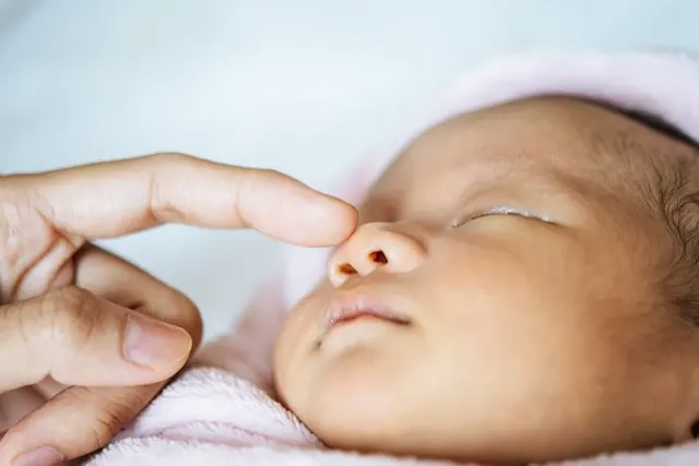 Neugeborenes Baby schläft friedlich, sanfte Berührung an der Nase.