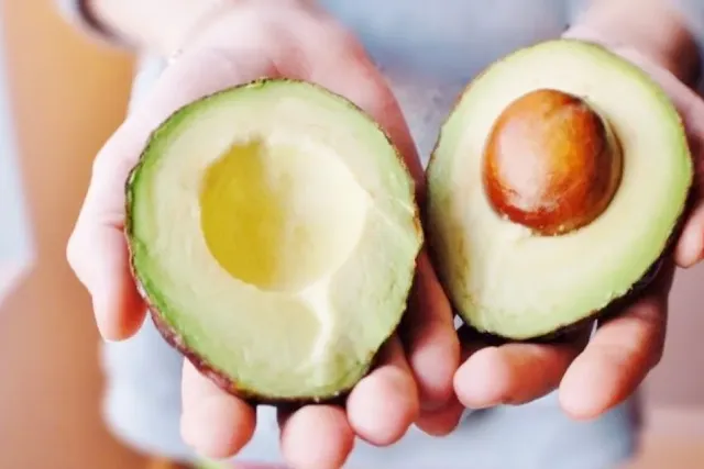 Frau hält aufgeschnittene Avocado