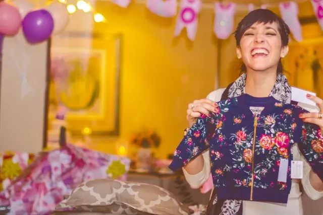 Lachende Schwangere bei Babyparty hält Geschenk hoch