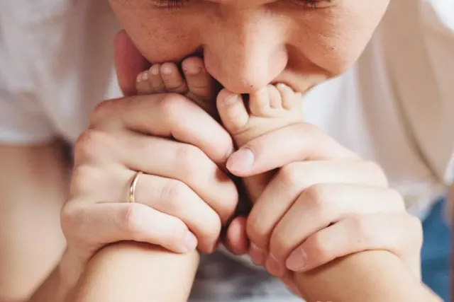 Junge Mutter küsst die Füße ihres Säuglings