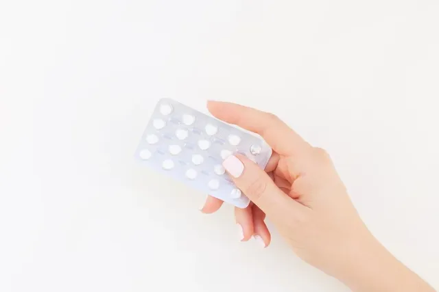 Hand hält eine Packung Antibabypillen vor weißem Hintergrund.