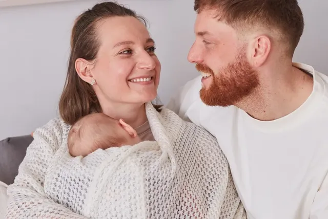 Glückliche junge Familie mit Neugeborenem eingehüllt in eine Decke.