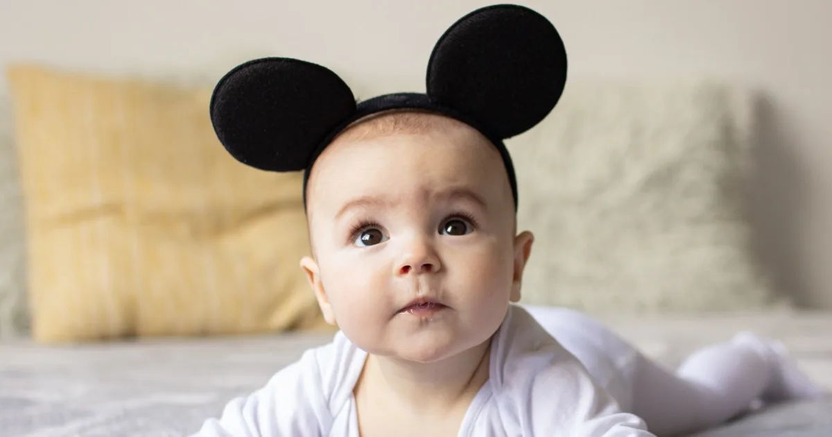 Baby mit schwarzem Mäuseohren-Stirnband liegt auf dem Bauch.