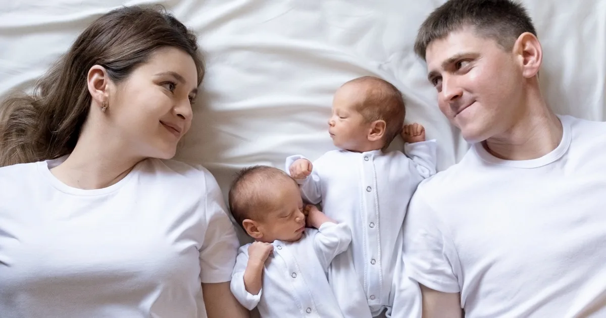 Glückliche Eltern liegen mit ihren neugeborenen Zwillingen im Bett.