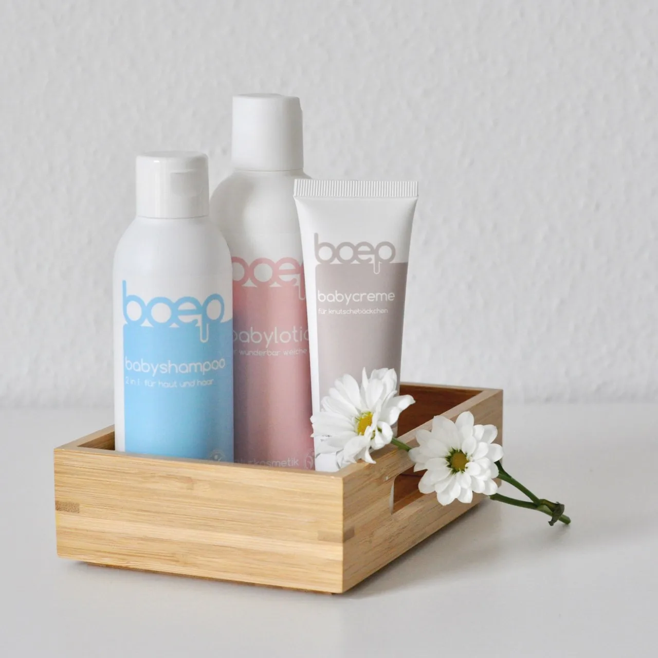 Babyshampoo, Babylotion und Babycreme in Holzbox mit Blumen.