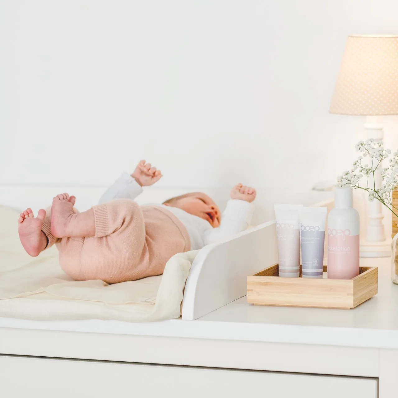 Neugeborenes Baby liegt auf Wickeltisch mit Babypflegeprodukten nebenan.