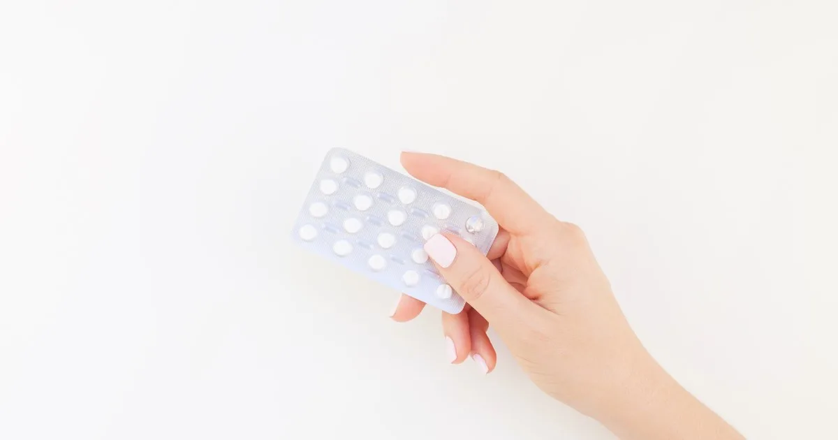 Hand hält eine Packung Antibabypillen vor weißem Hintergrund.