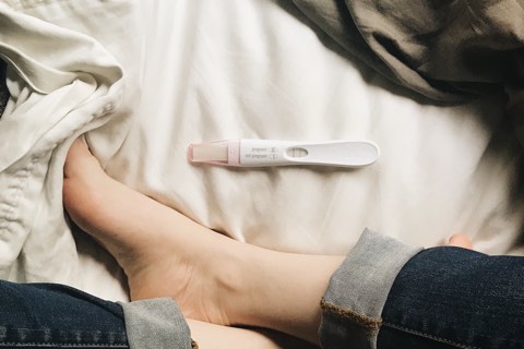 Frau mit positiven Schwangerschaftstest im Bett