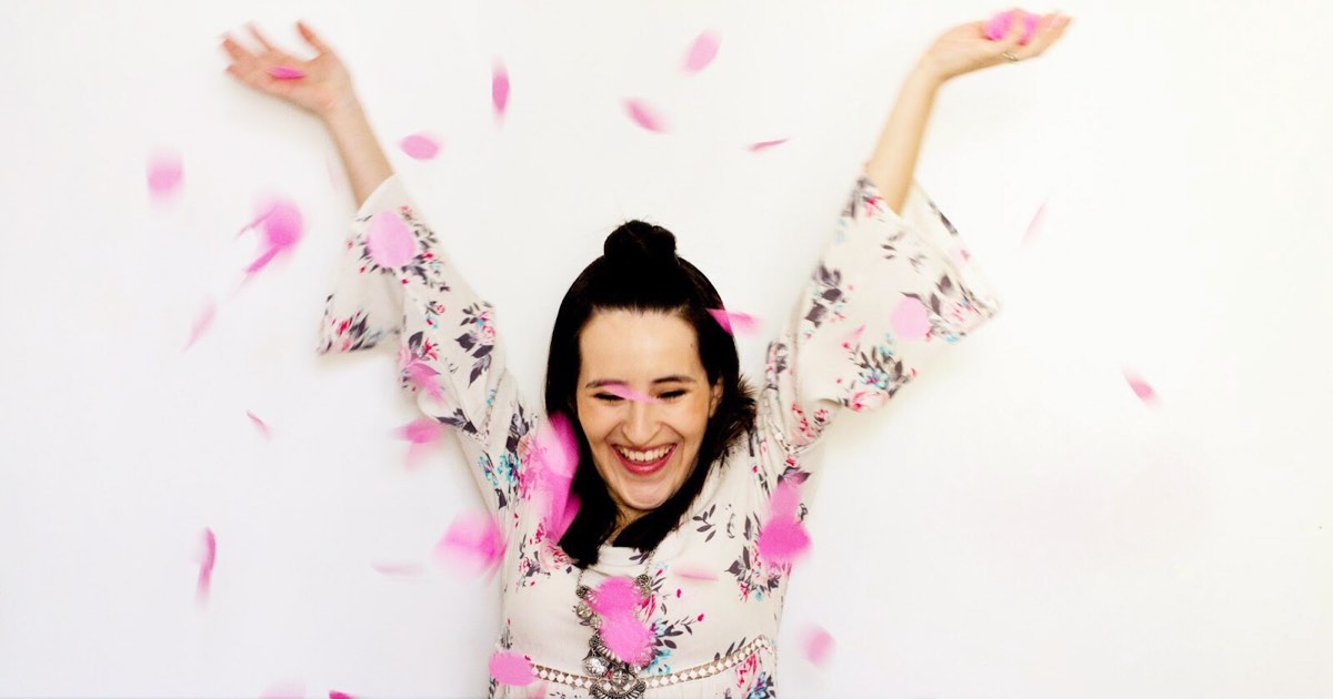 Lachende schwangere Frau mit rosa Confetti bei Babyparty