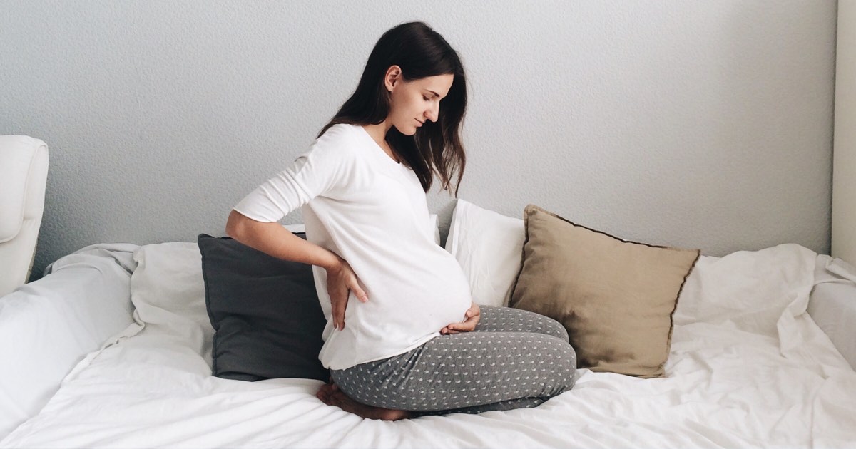 Schwangere Frau im Bett mit Rückenschmerzen