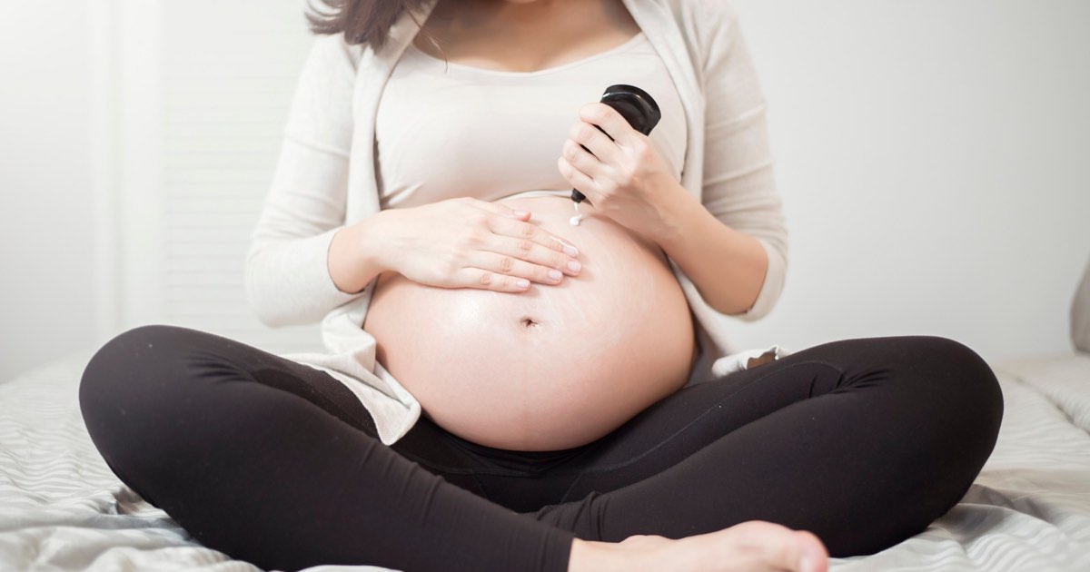 Schwangere Frau cremt sich den Bauch gegen Schwangerschaftsstreifen ein