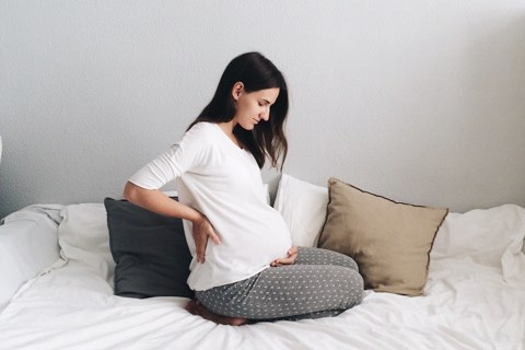 Schwangere Frau mit Rückenschmerzen im Bett