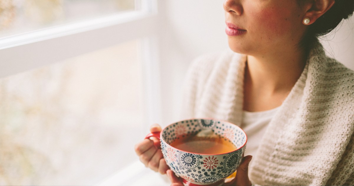 Frau trinkt Tee aus großer bunter Tasse