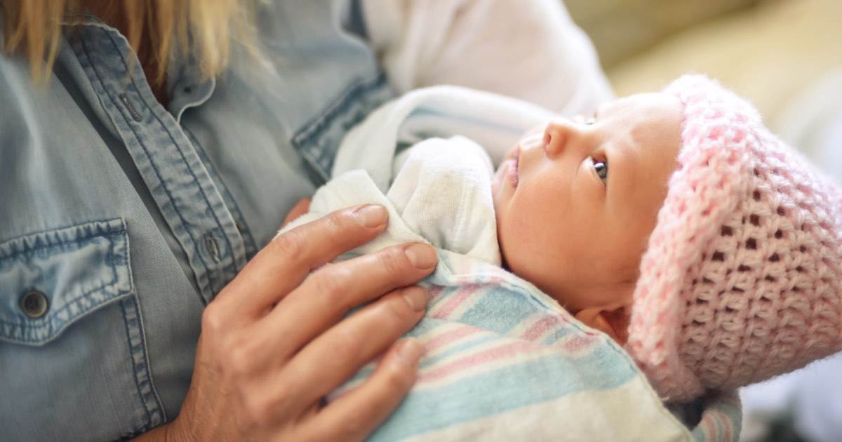 Frau hält Neugeborenes mit Häubchen