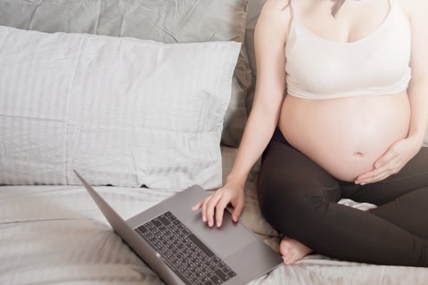 Schwangere Frau recherchiert mit Laptop auf Couch