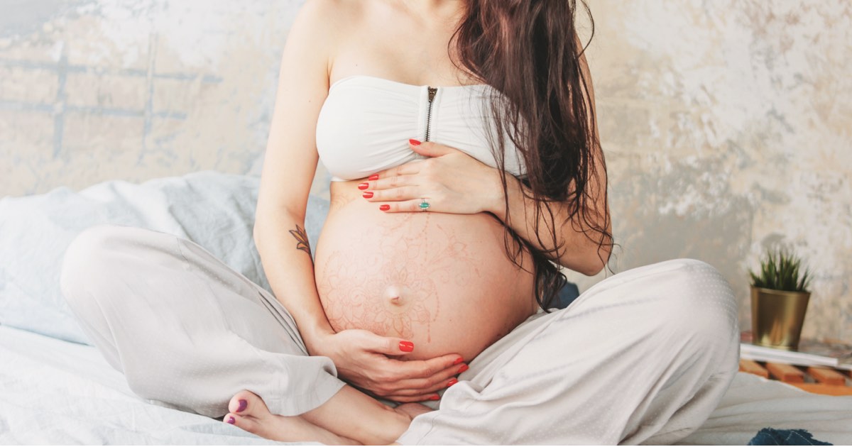 Schwangere sitzt im Bett und hält ihren Bauch