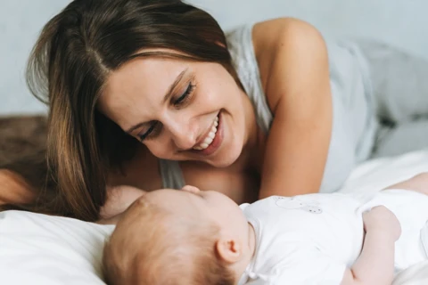 Mutter mit Baby im Bett lachend