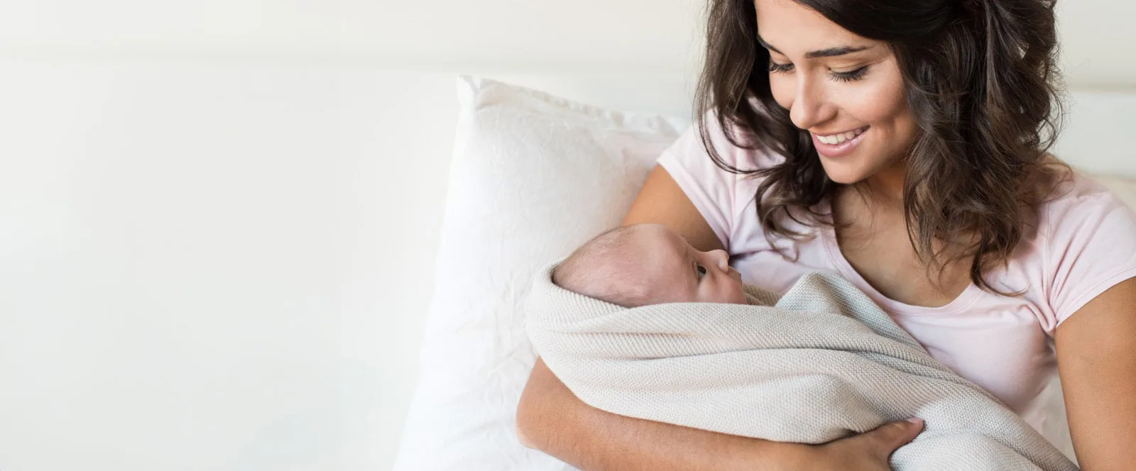 Mutter hält ihr Baby liebevoll in einer Decke gewickelt im Arm.