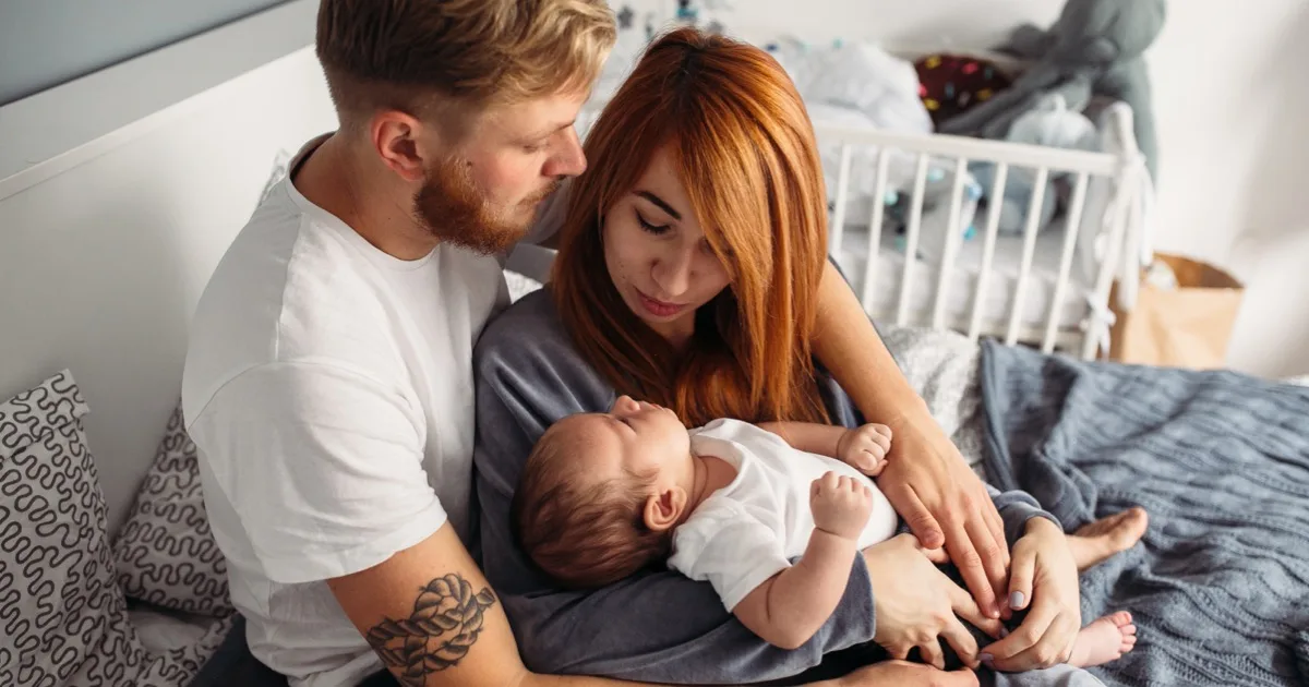 Junge Eltern halten ihr Baby liebevoll im Arm im Schlafzimmer.