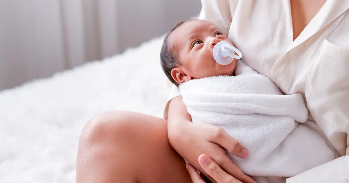 Neugeborenes Baby mit Schnuller wird von Mutter liebevoll gehalten.