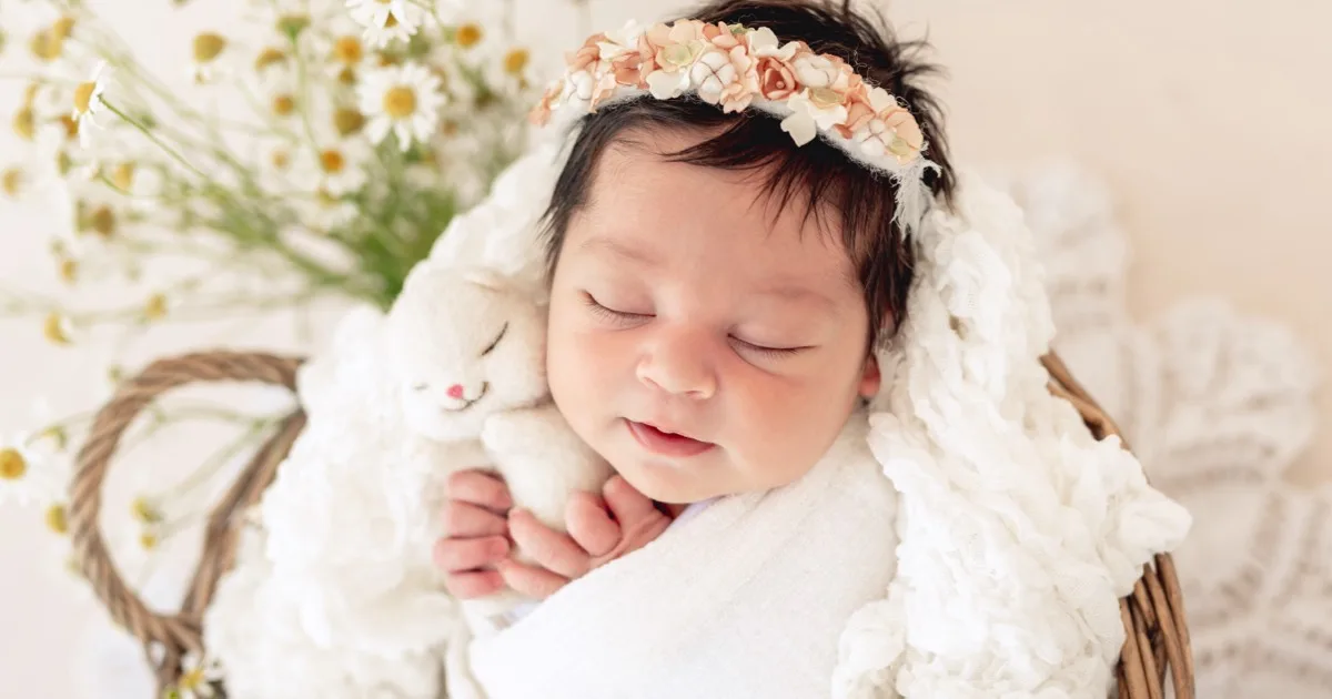 Neugeborenes Baby schläft mit Kuscheltier und Blumenkranz.
