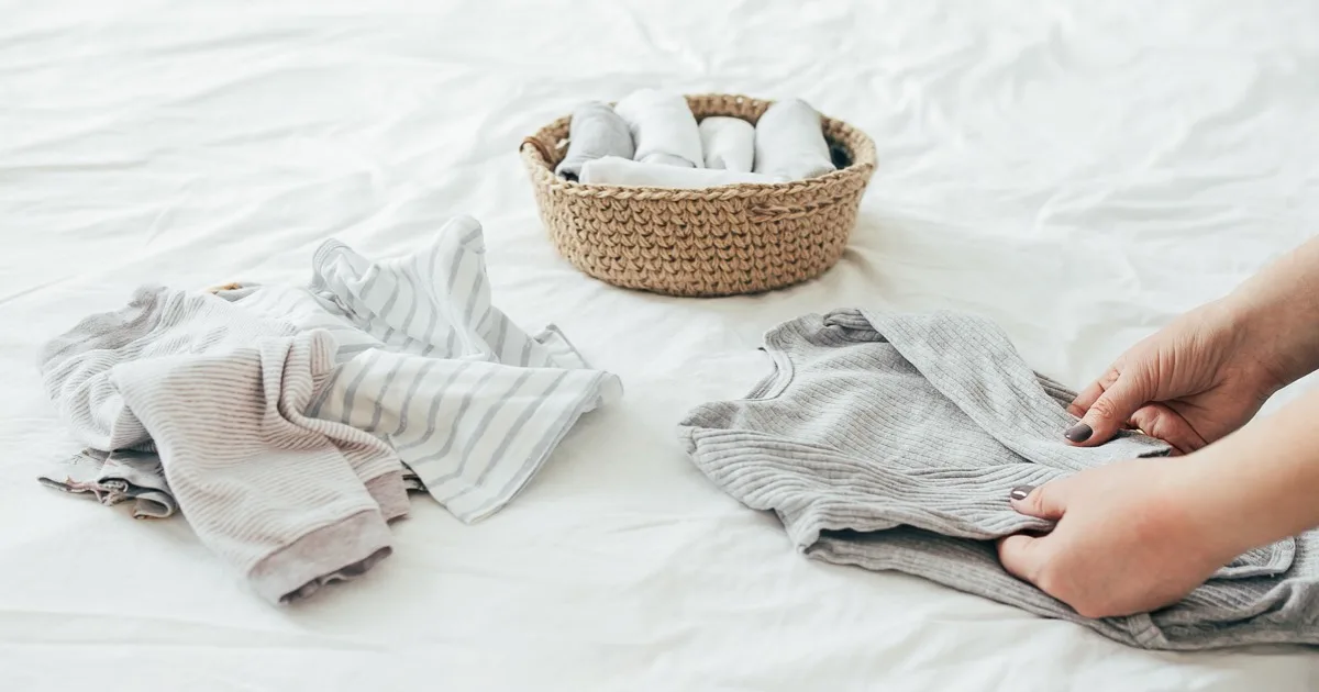 Babybekleidung falten und ordnen auf einem Bett mit Wickeltücherkorb.