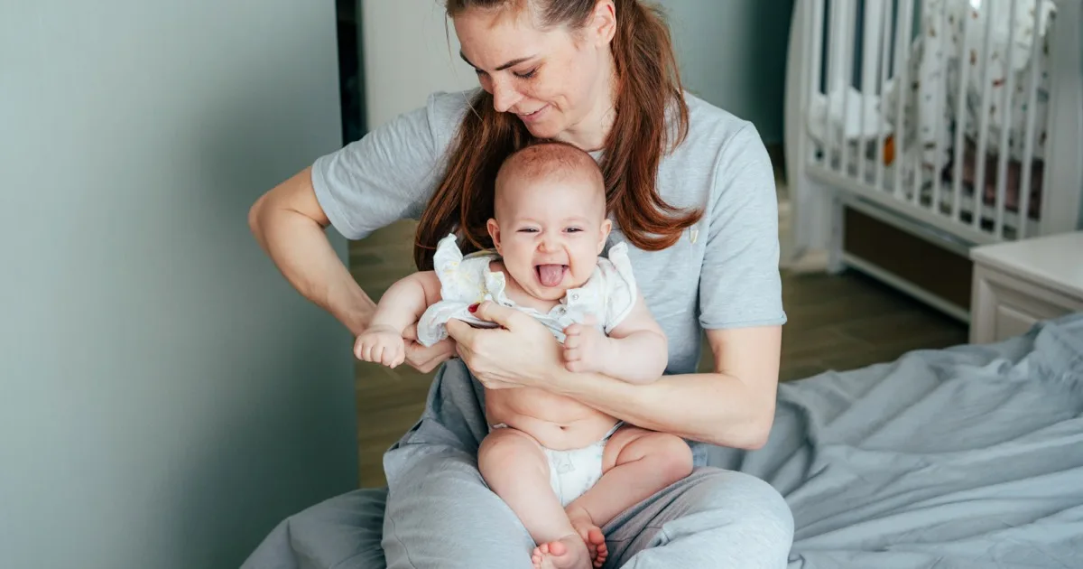 Mutter spielt lachend mit Baby auf dem Bett im Kinderzimmer.