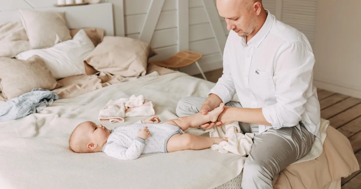 Vater massiert liebevoll die Füße seines Babys auf dem Bett.