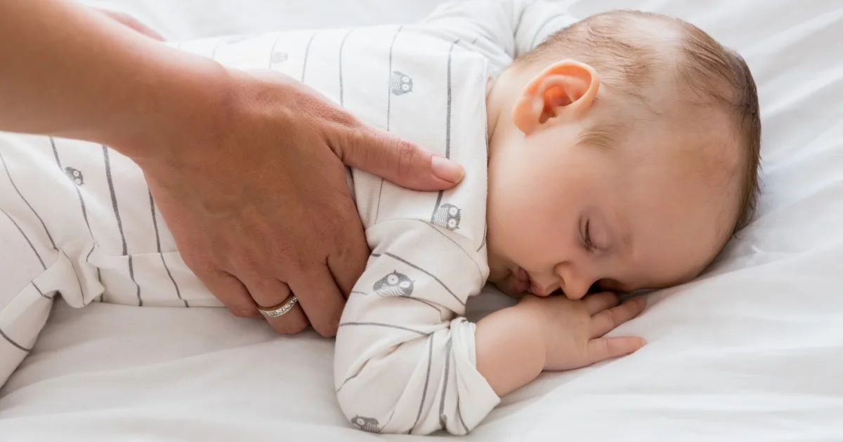 Schlafendes Baby wird sanft vom Elternteil gehalten.