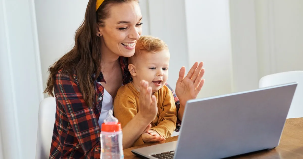 Frau mit Kleinkind freut sich beim Videochat am Laptop zu Hause.
