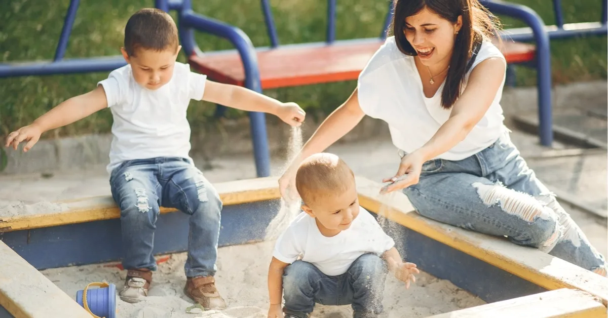 Mama spielt mit zwei Kleinkindern im Sandkasten im Park.