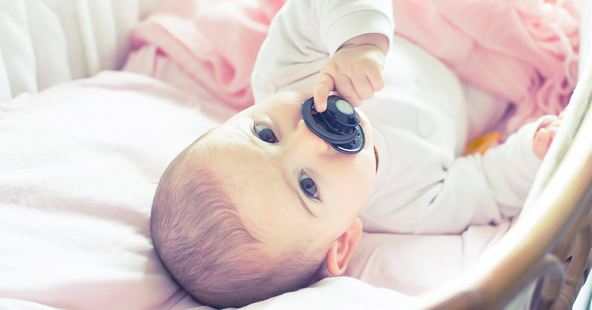 Baby mit Schnuller im Mund sieht in die Kamera