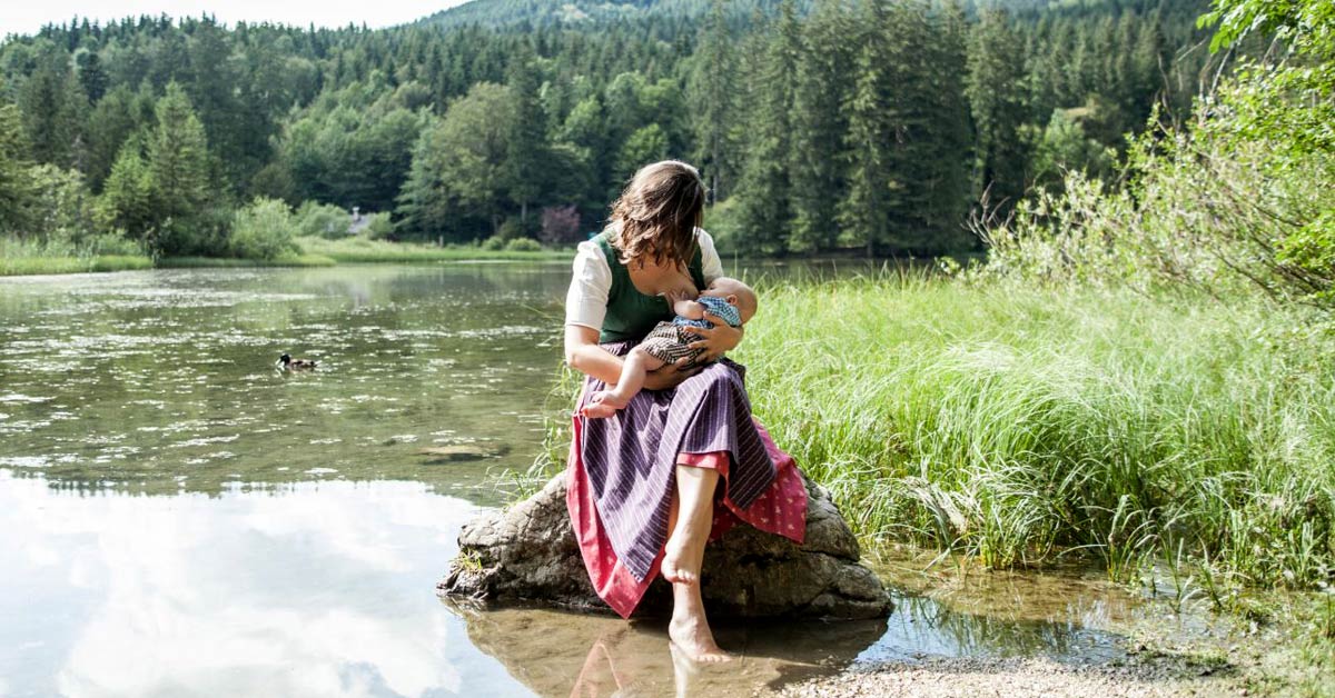 Mutter stillt ihr Baby in Tracht an einem Bergsee
