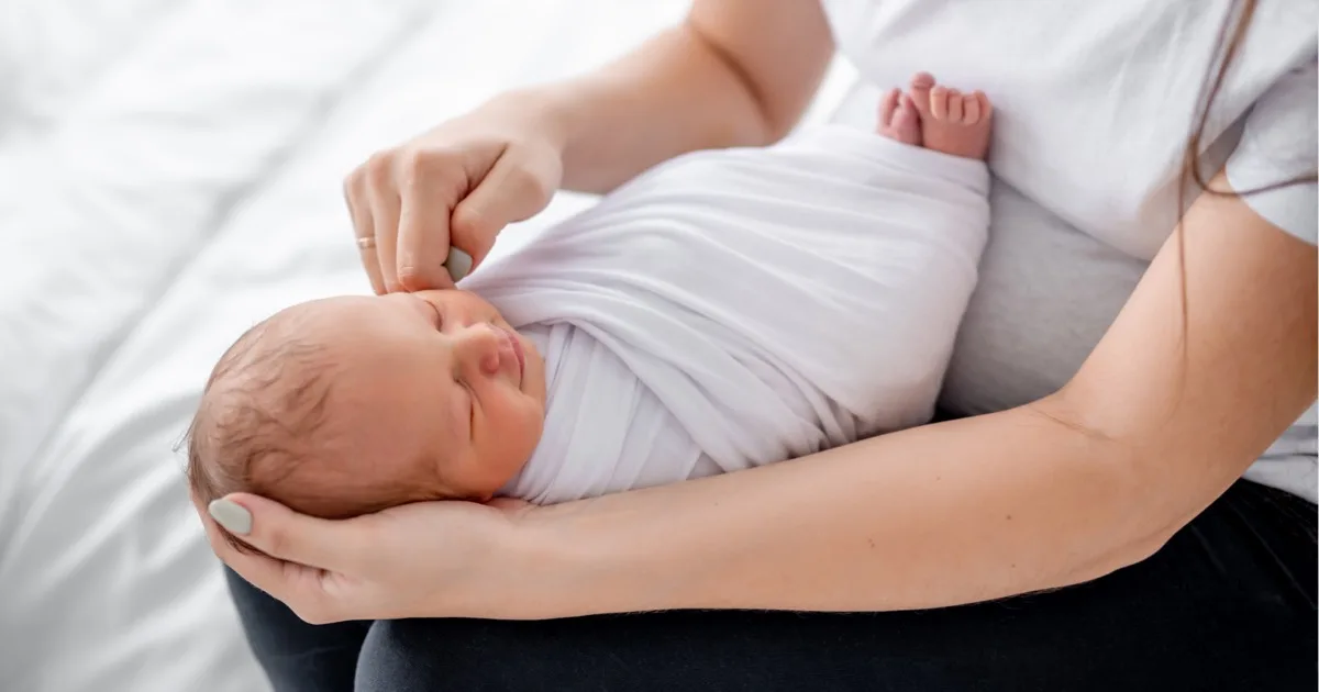 Neugeborenes Baby liebevoll gewickelt im Arm der Mutter