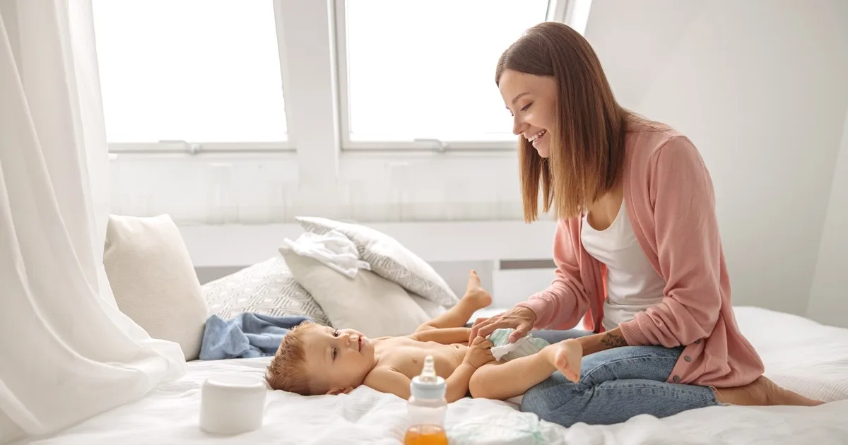 Mutter wechselt lächelnd Windel bei Baby auf dem Bett in hellem Schlafzimmer