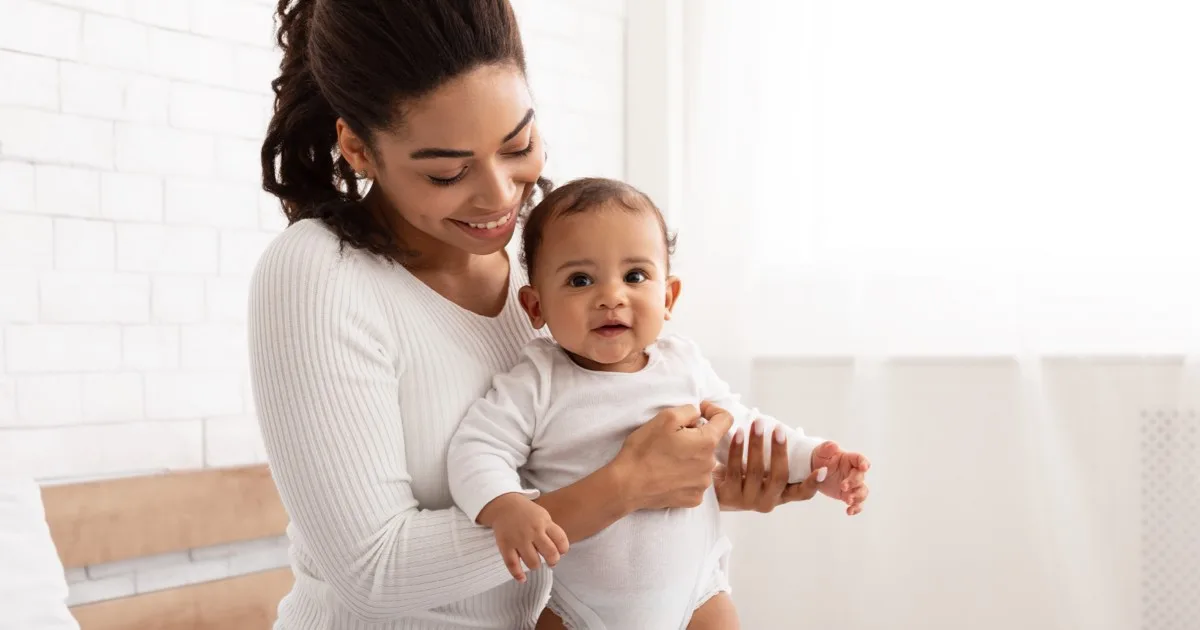 Mutter hält lächelnd ihr Baby im hellen Wohnzimmer