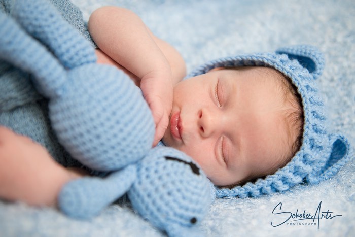 Baby Bub liegt schlafend im Bett mit blauem Kuscheltier