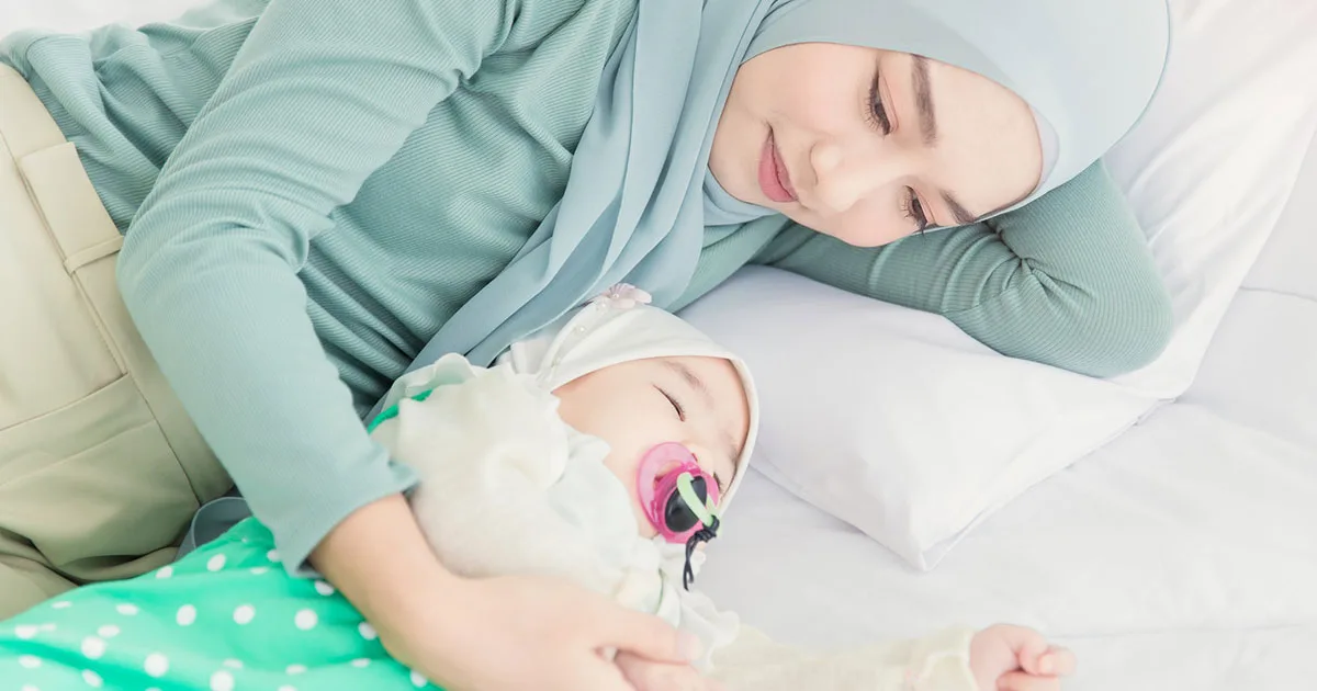 Mutter legt sich liebevoll neben schlafendes Baby mit Schnuller.