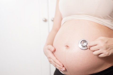 Schwangere hält Stetoskop an Bauch